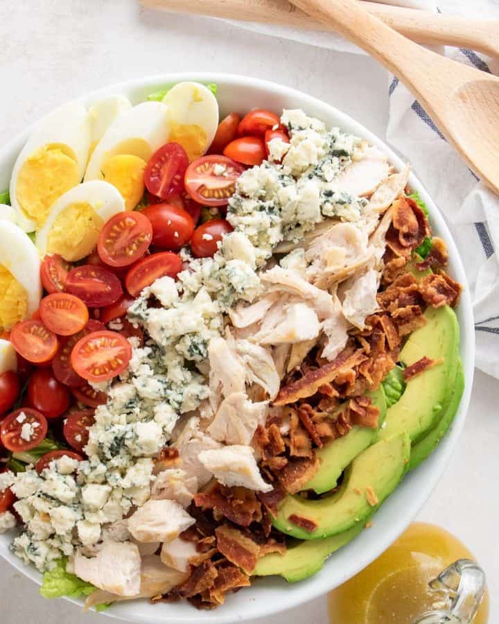 Cobb salad overhead with avocado, eggs, tomatoes, blue cheese crumbles, bacon, and chicken in a bowl.