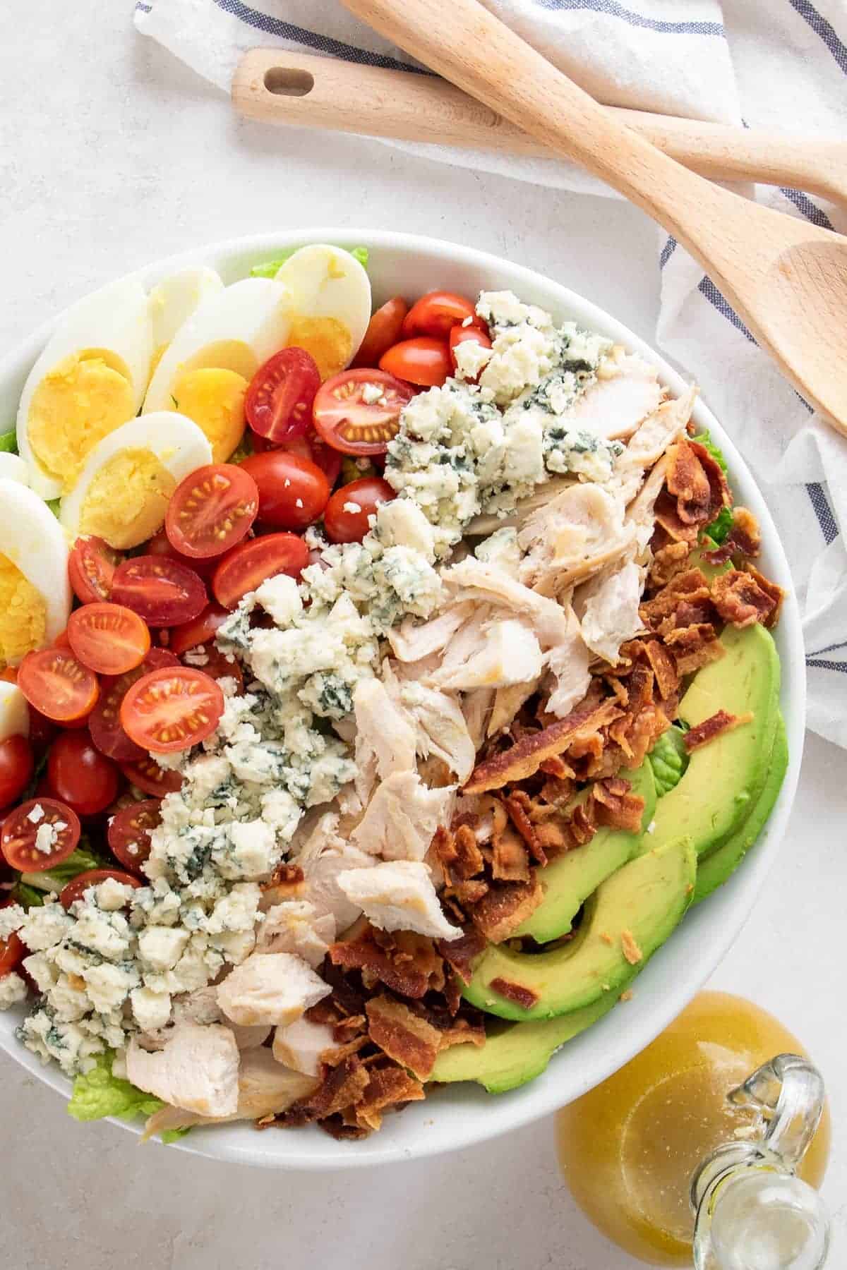 Cobb salad overhead with avocado, eggs, tomatoes, blue cheese crumbles, bacon, and chicken in a bowl.