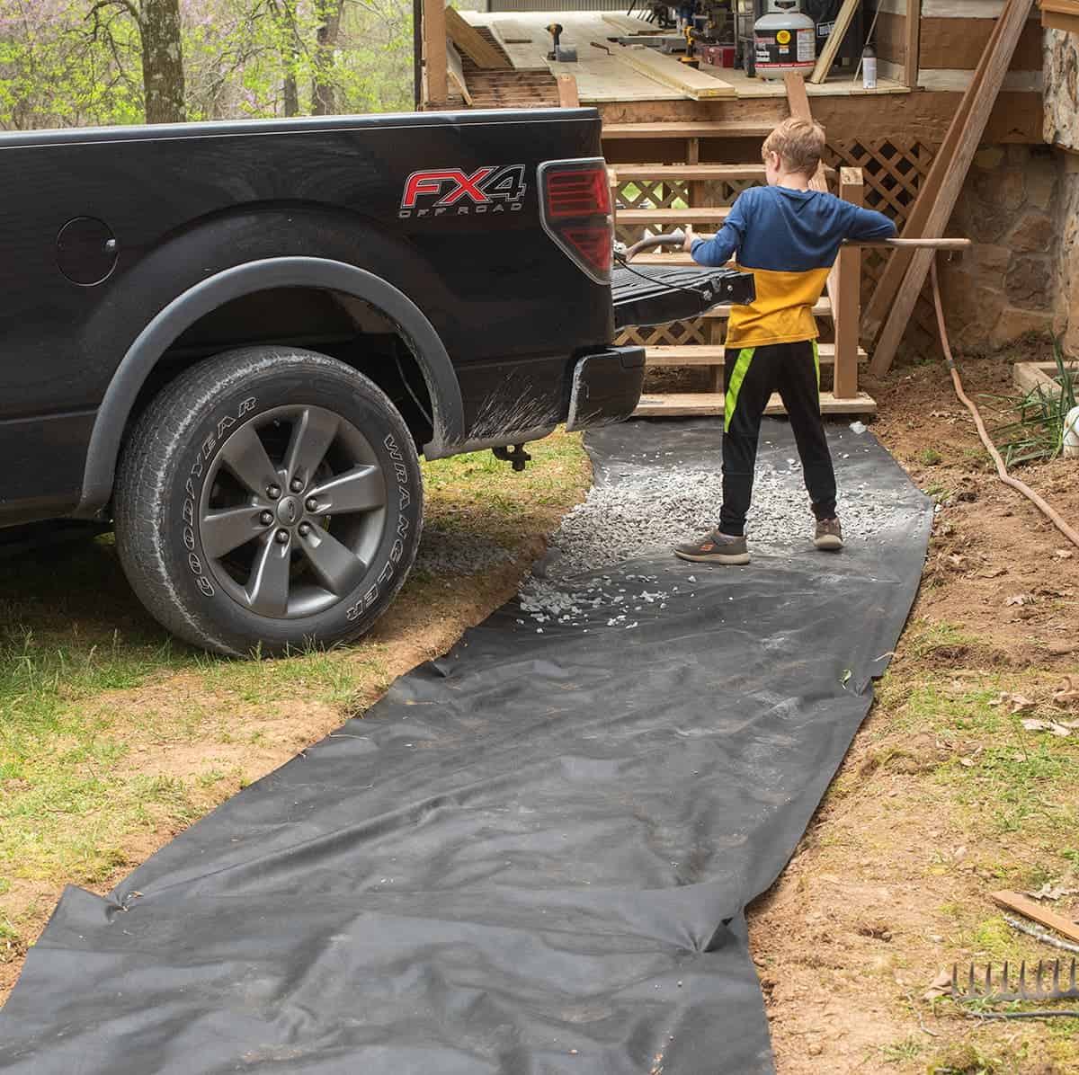 Shoveling gravel over landscape tarp to create a walkway. Gravel is being shoveled by hand directly from a pickup truck bed.
