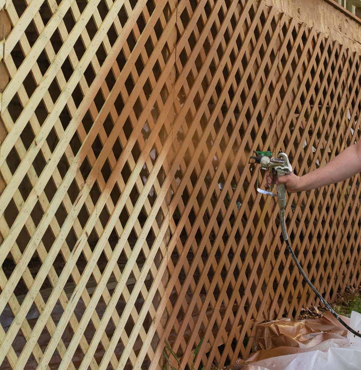 Photo of lattice painting in progress using paint sprayer. Person's hand is visibly applying finish with a paint sprayer.