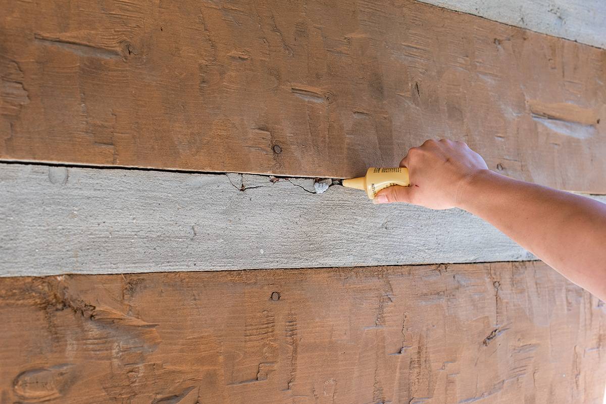 A woman using a tube of concrete patch to fill in large cracks in masonry.
