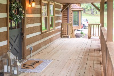 A rustic log cabin house with grey front door on a large, enclosed wood deck.