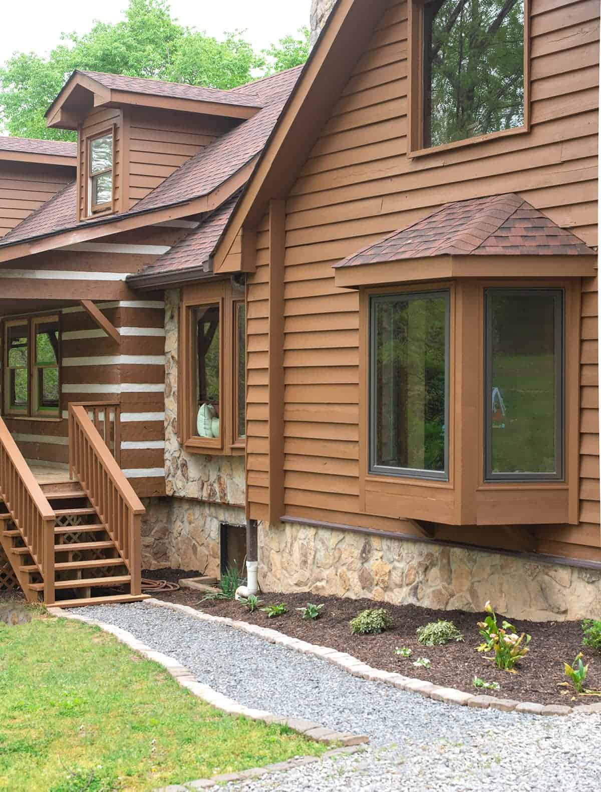 Front of craftsman log cabin house with bay window and staircase that are stained.