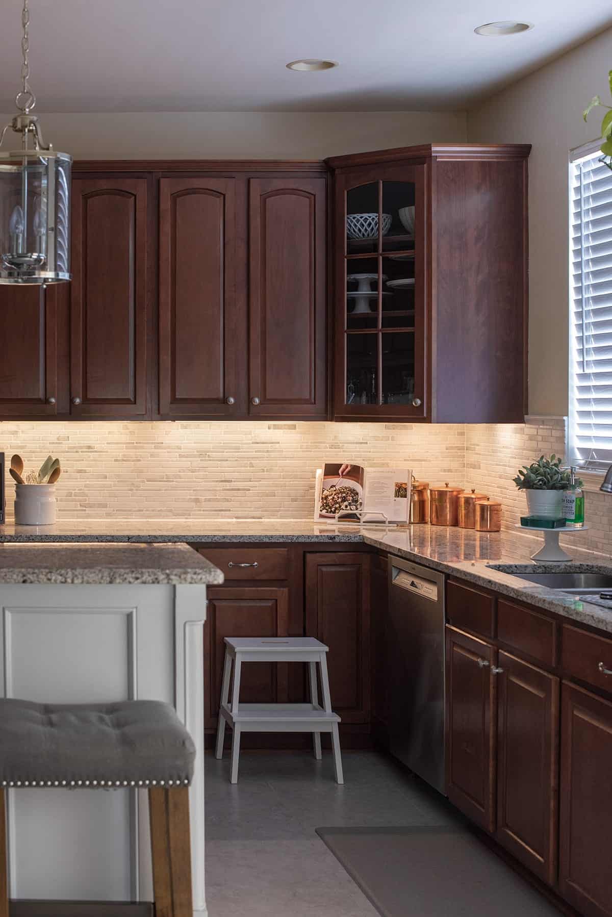 LED under cabinet lighting against gray and white tile back splash and dark cabinets. 