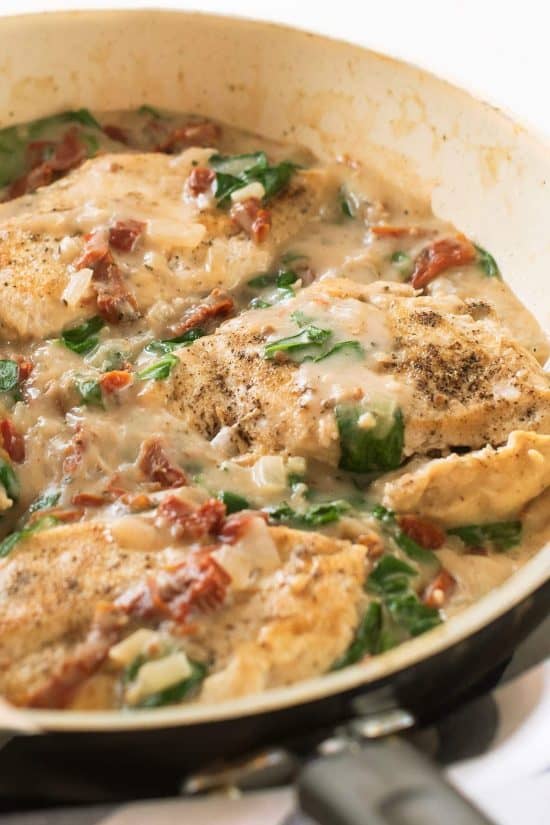 Tuscan chicken breasts smothered with sun dried tomatoes and spinach in a creamy sauce in a skillet.