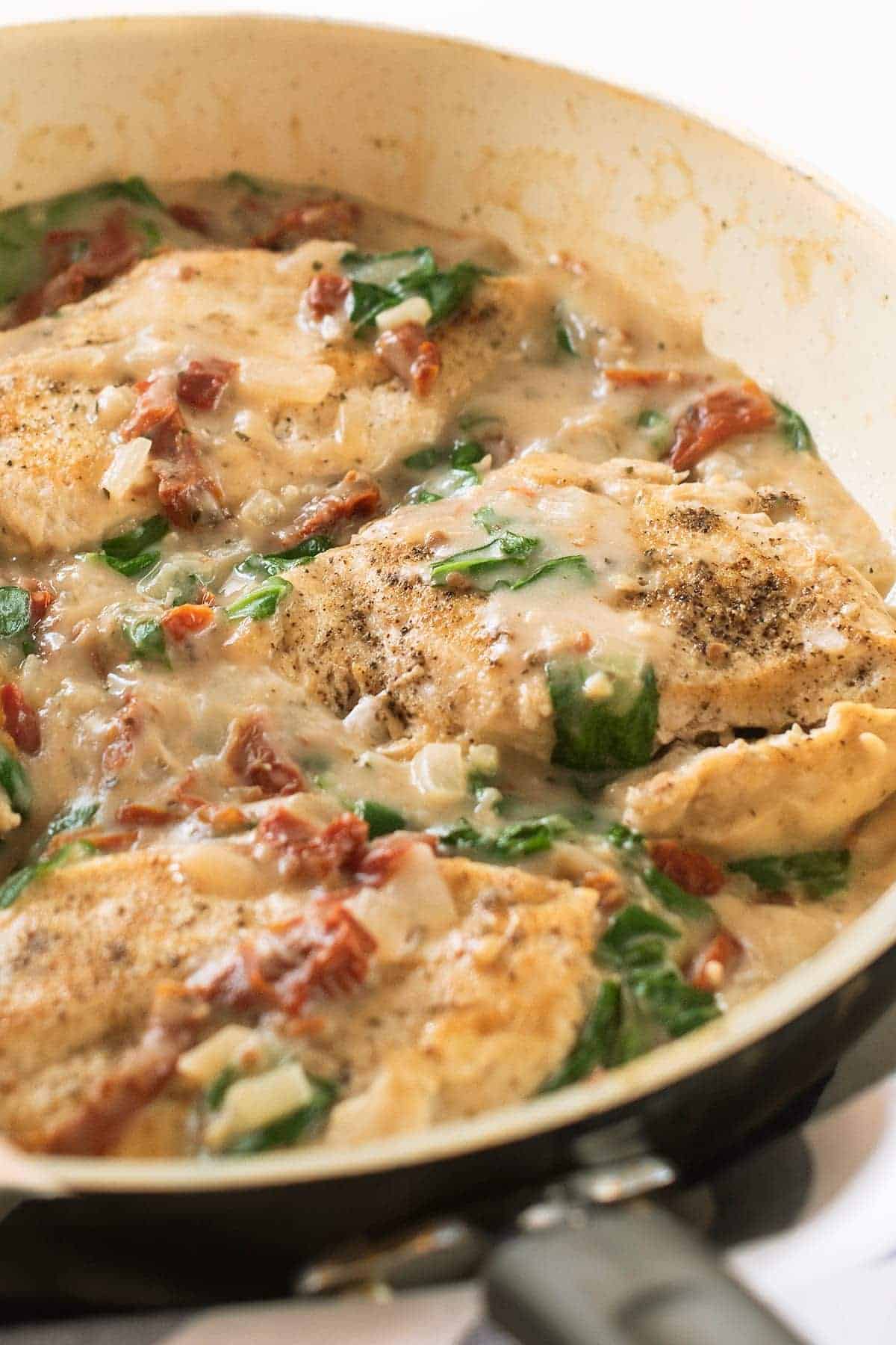Keto Tuscan Chicken Recipe with Coconut Milk. Spinach, seasoned chicken and sun-dried tomatoes in a pan.