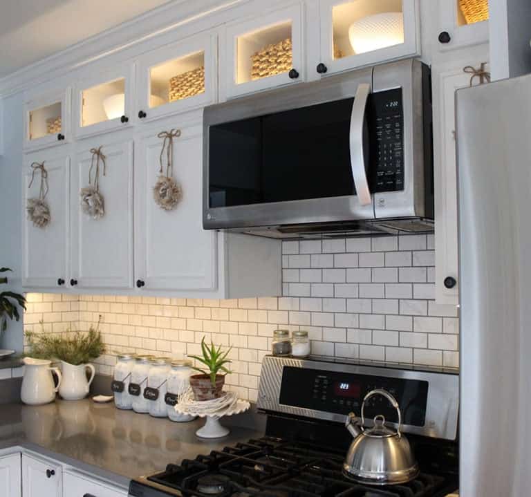 LED Cabinet Lighting against white subway tile back splash. Modern gray counter tops and white cabinets. White farmhouse style decor accents.