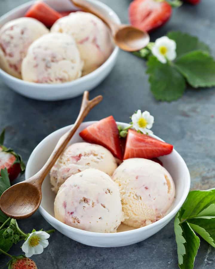 Two bowls of strawberry cheesecake ice cram with scoops in them and a wooden spoon.