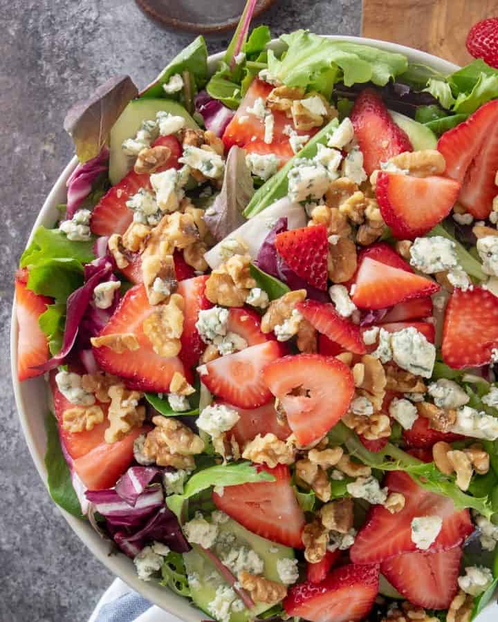 Strawberry spinach salad with feta crumbles and pecans in a salad bowl.
