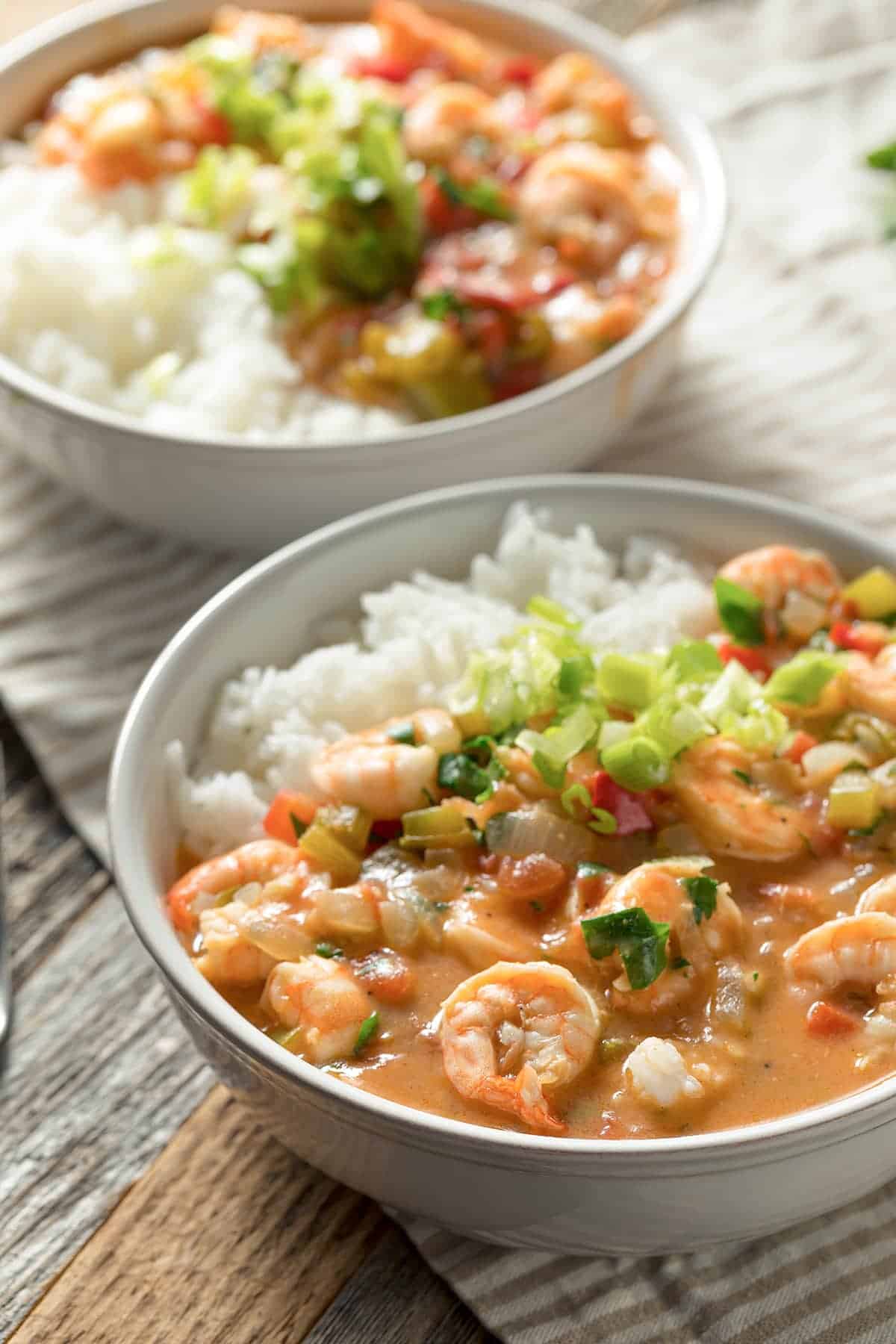Two generous bowls of cajun shrimp etoufee served over white rice with sliced green onions. 