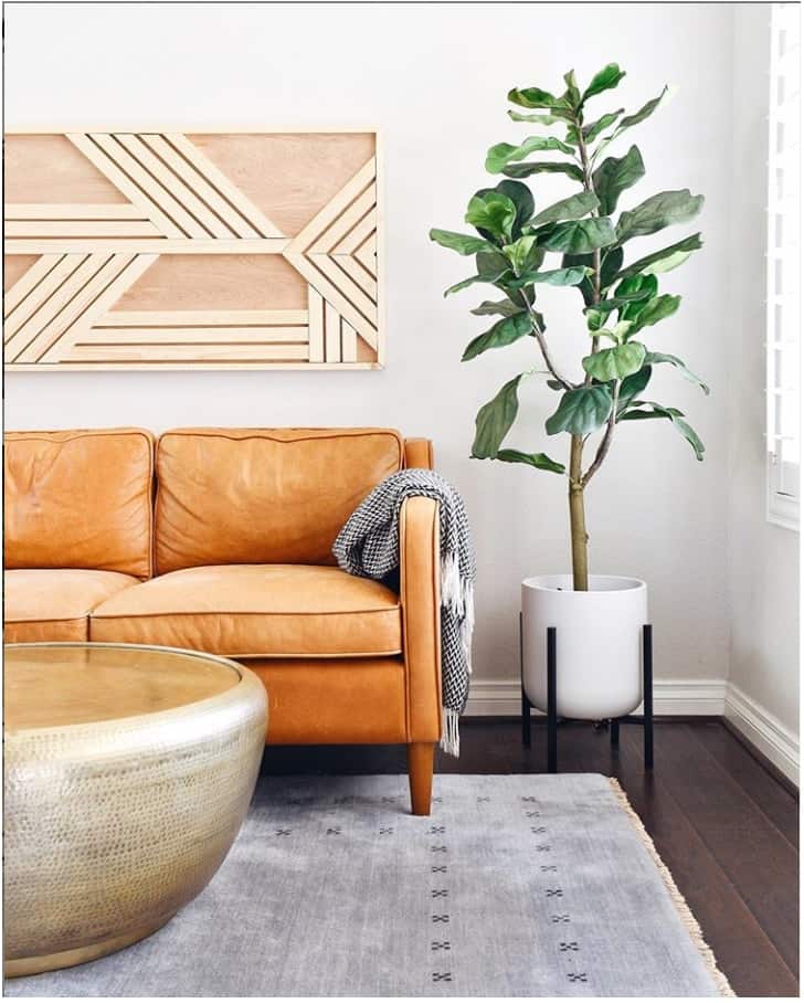 Modern living room with geometric wooden wall art piece above couch, potted plant, neutral area rug, and round metal coffee table. 