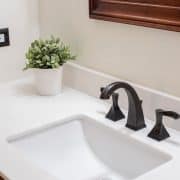 Updated white counter top with square style sink and modern farmhouse style hardware. Light neutral wall color and a potted succulent.