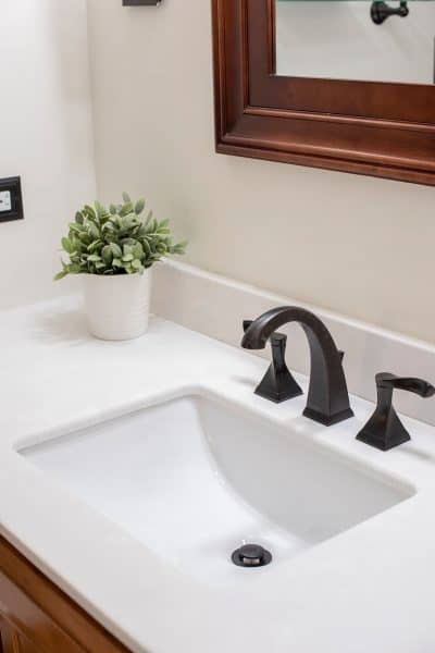 Updated white counter top with square style sink and modern farmhouse style hardware. Light neutral wall color and a potted succulent.