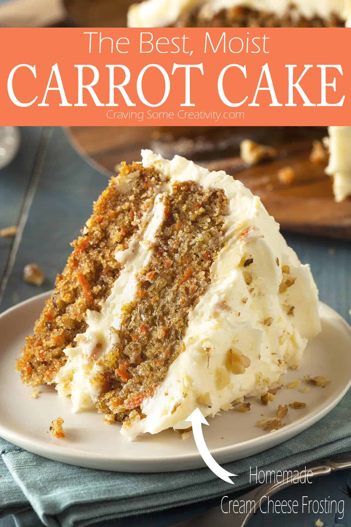 Double layered slice of cream cheese frosted carrot cake on white plate over folded blue towel next to full cake on wooden tray. 