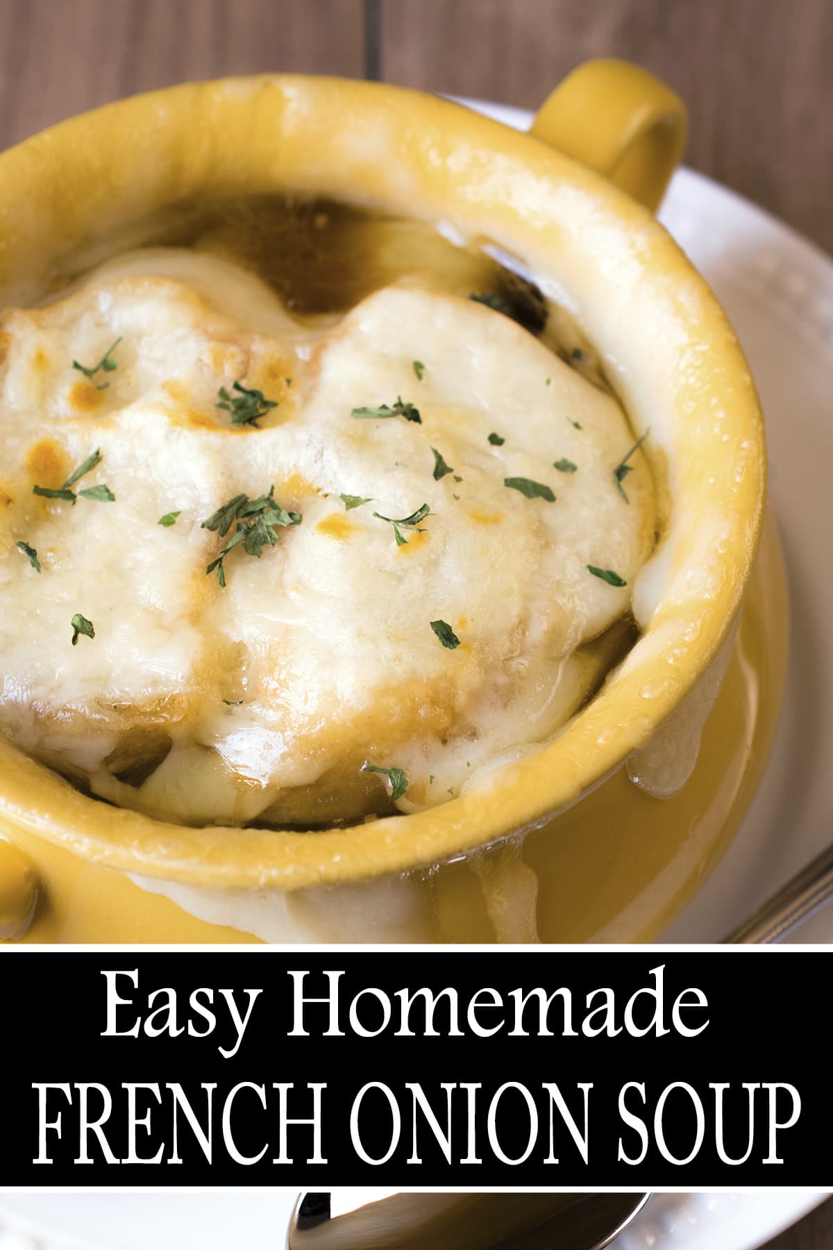 Cheesy French onion soup in a small yellow soup crock on white plate, garnished with parsley. 