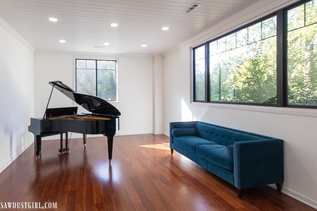 White plank drop-down ceilings with recessed lights in brightly lit great room with large windows, piano and turquoise settee. 
