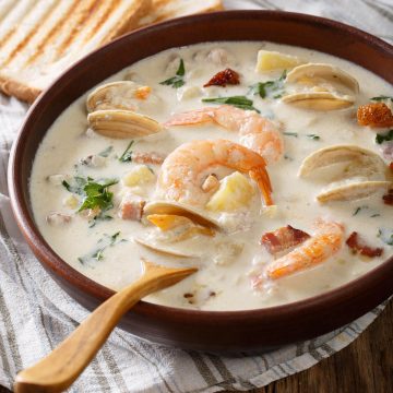 A bowel of creamy Seafood Chowder soup with shrimp and mussels. Wooden spoon and toasty bread on the side.