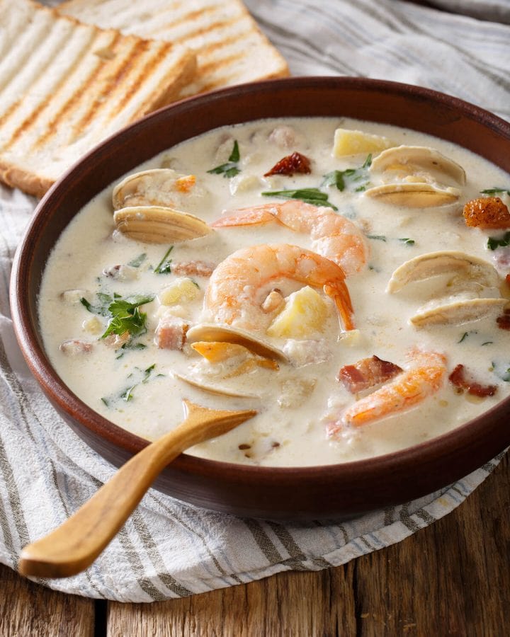 A bowel of creamy Seafood Chowder soup with shrimp and mussels. Wooden spoon and toasty bread on the side.