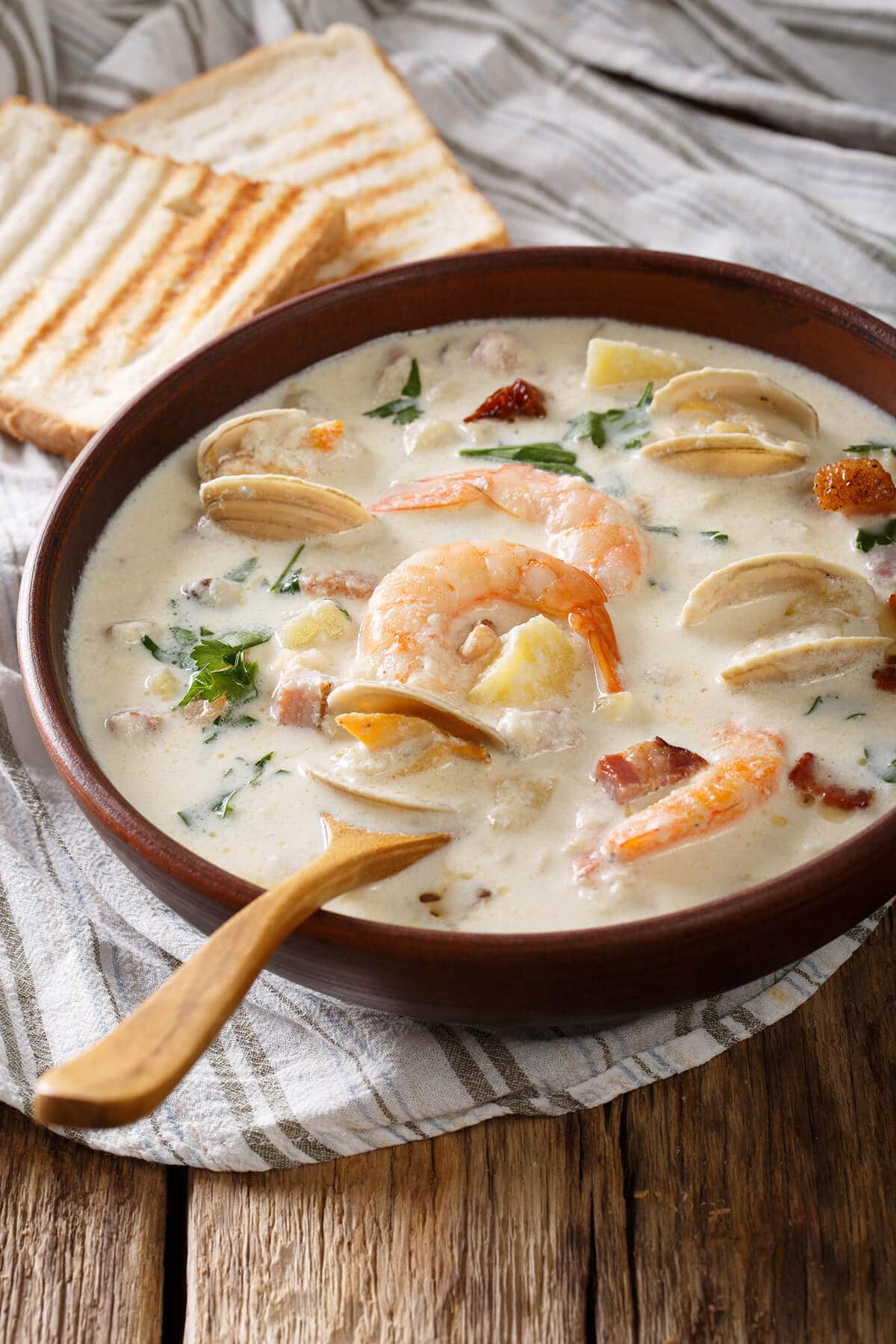 A bowl of creamy Seafood Chowder soup with shrimp and mussels. Wooden spoon and toasty bread on the side.