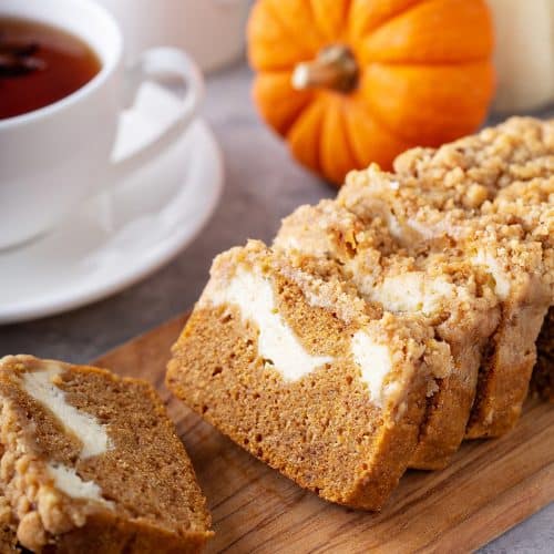 Sliced Pumpkin Cream Cheese Bread on a wood platter with mini pumpkins in the background.