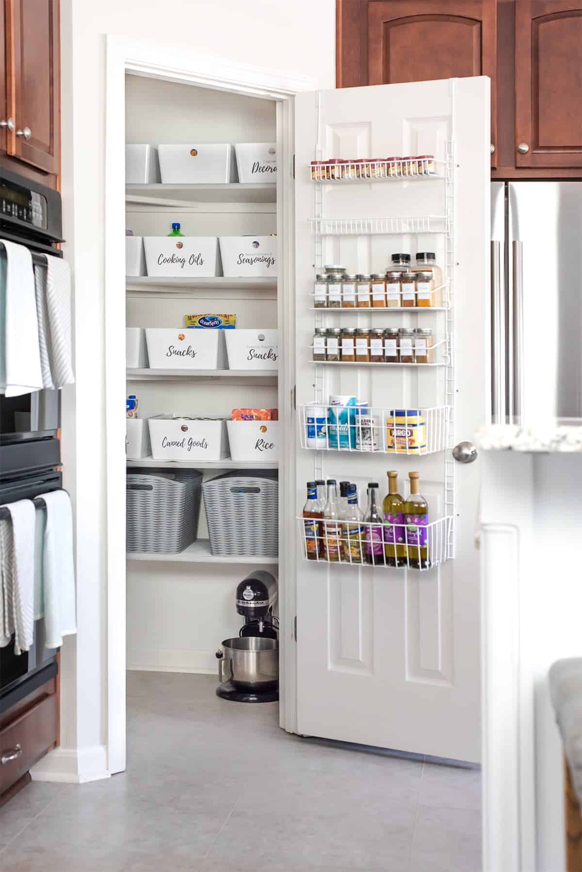 Full size shot of organized pantry. Over-the-door storage rack for spices. Labeled uniform bins on shelves.