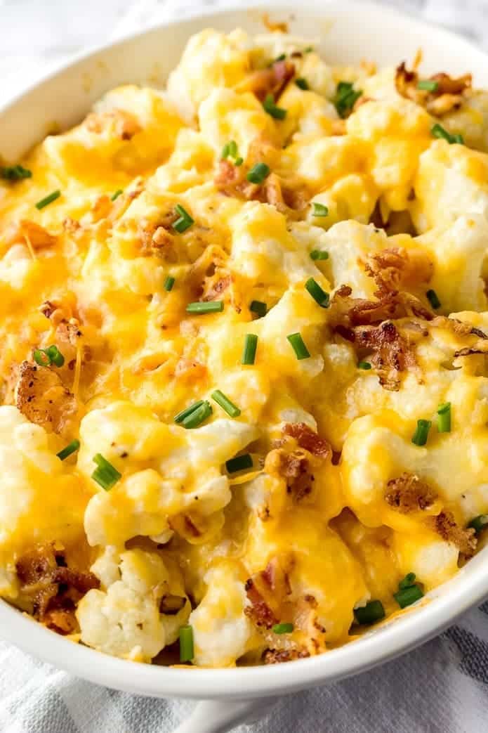 Loaded cauliflower casserole with melted cheese, topped with bacon and chives in white bowl. 