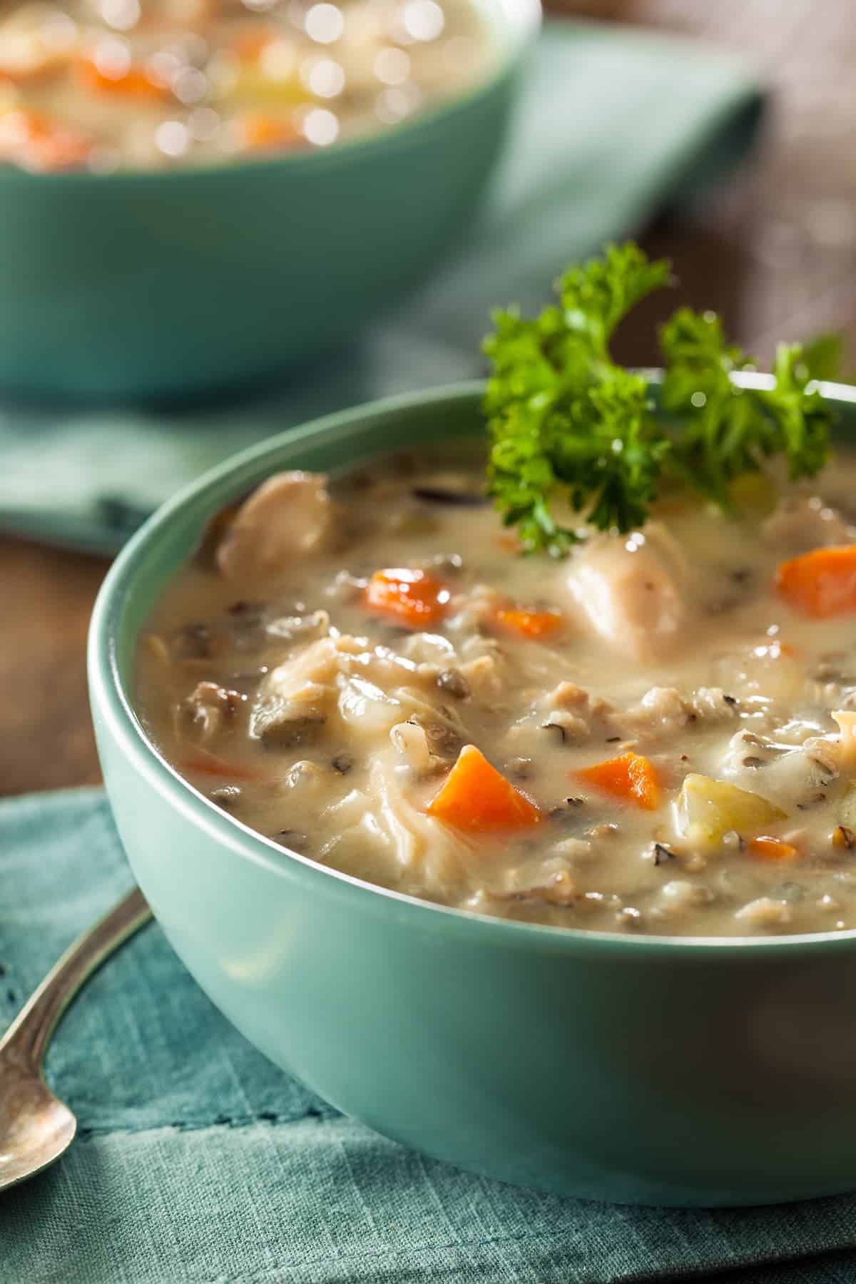 Texture Closeup of Creamy Chicken and wild rice soup with aqua soup bowl and spoon on wood board background.