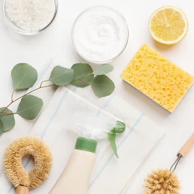Picture of supplies for natural glass cleaner like eucalyptus, halved lemon, baking soda, salts, linen dish towels and sisal cleaning tools.