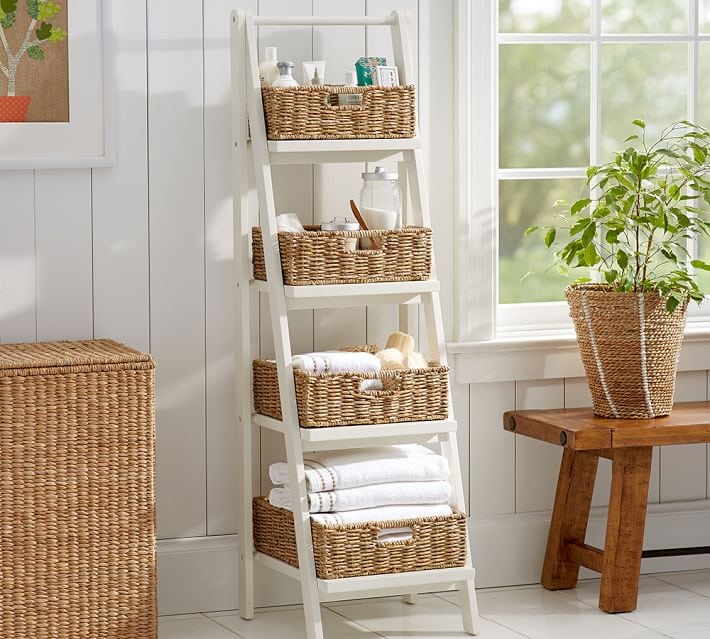 White ladder shelves filled with baskets and toiletries while leaning again white wall.