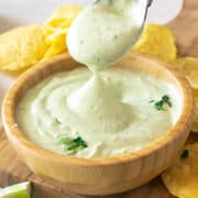 Avocado crema dip being spooned out of a small bowl.