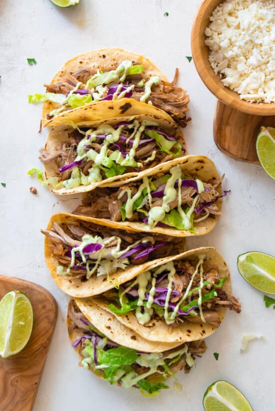 Carnitas Tacos with slaw and sauce sprinkled on top. Tacos are laid out on a white background.