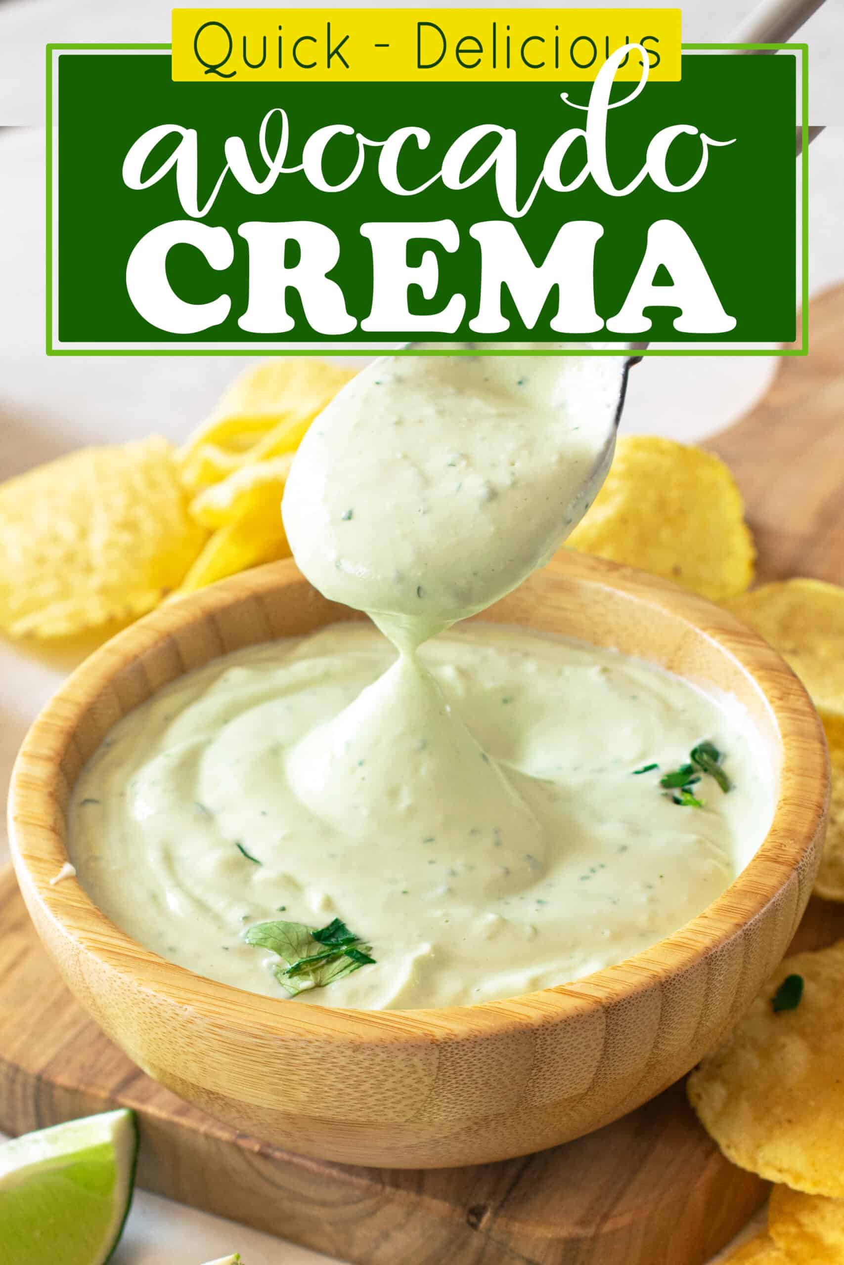 Avocado Crema in a bowl with spoon dipping into and tortilla chips sprinkled around.