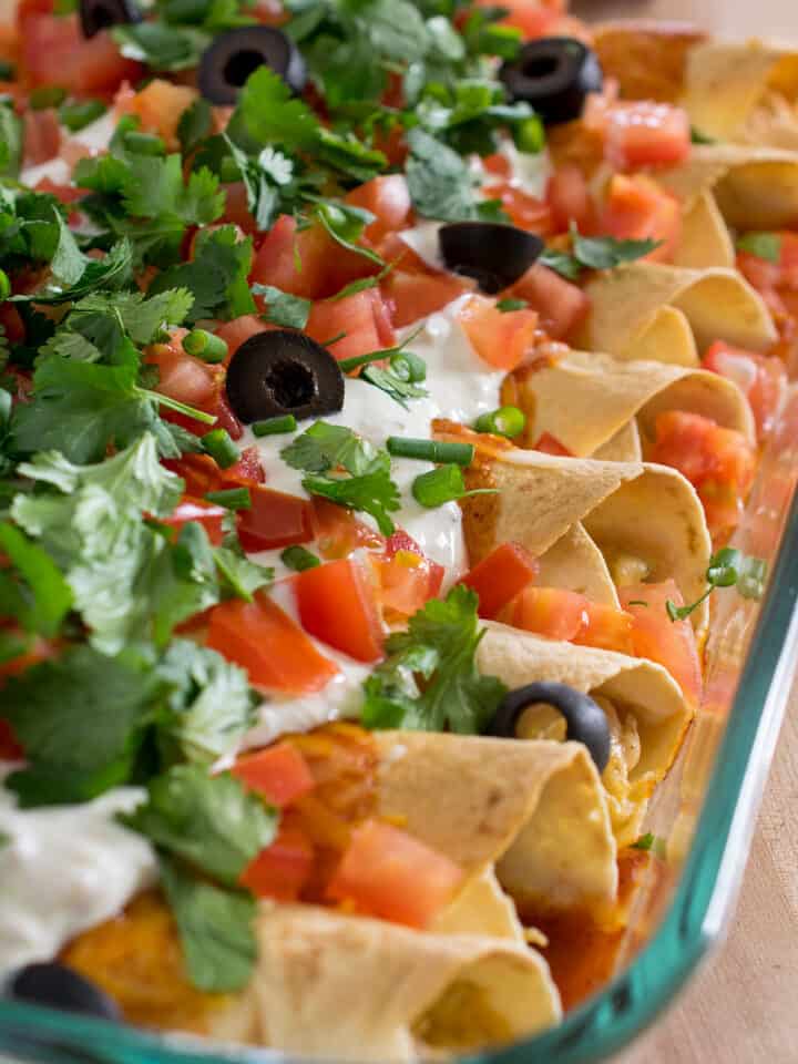 Cheesy chicken enchiladas in a glass dish with toppings.