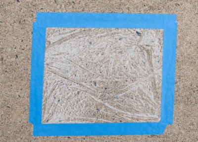 Concrete moisture test demonstration with plastic wrap and painter's tape on the floor.