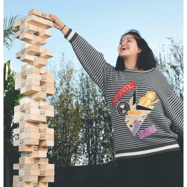 Girl reaching to the top of yard jenga stacking game.