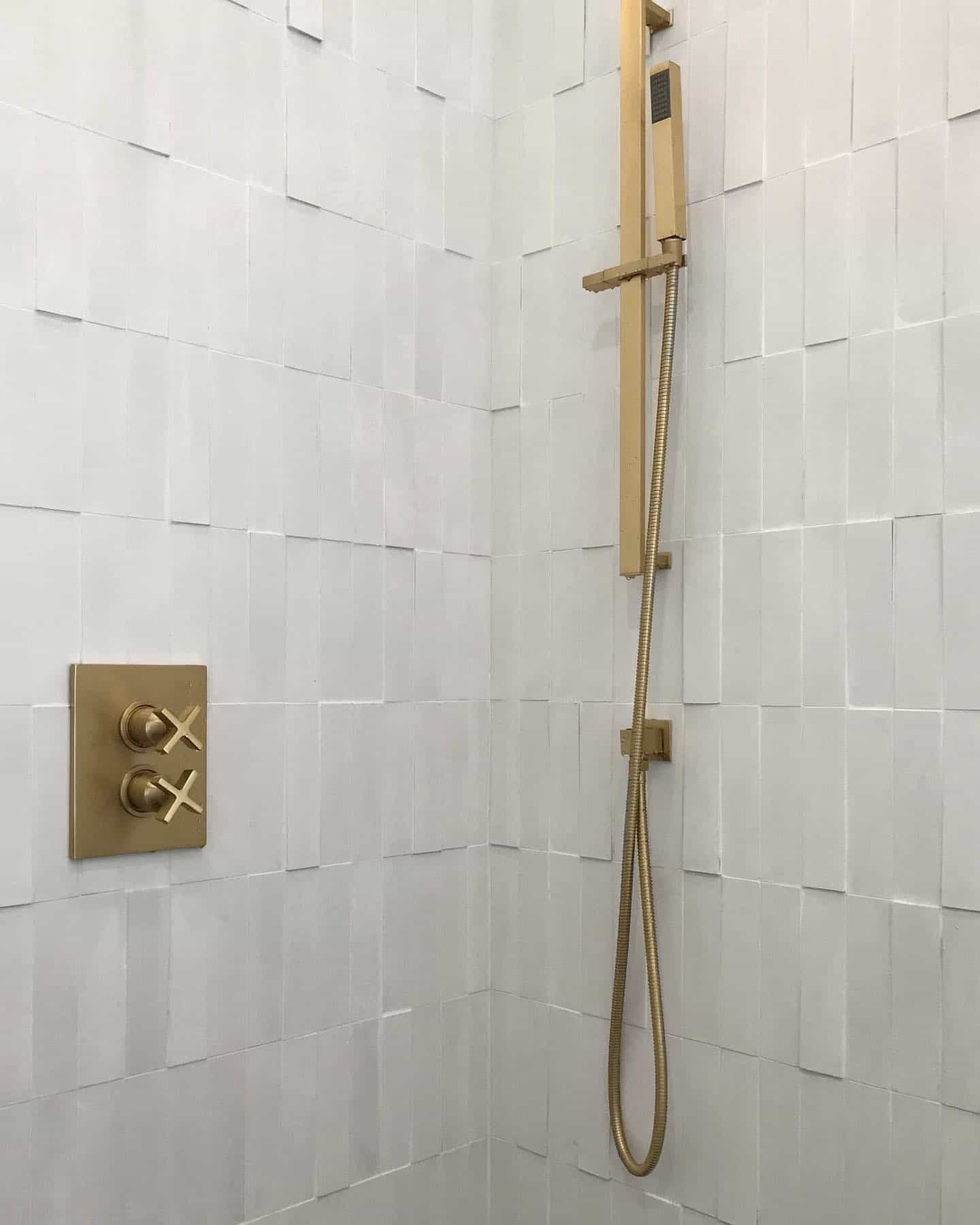 Vertical stack textured white tile in shower with brass accents including faucet and handles.