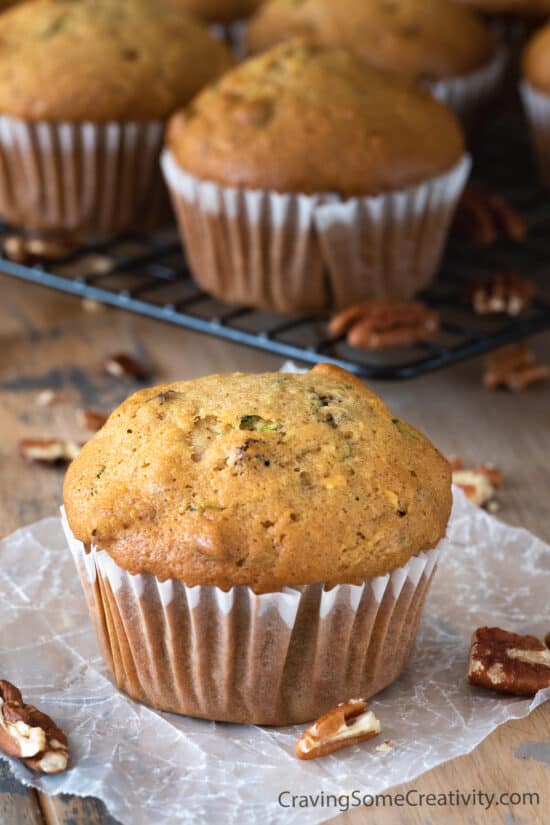 Zucchini Muffin in a paper wrapper with several muffins in the background.