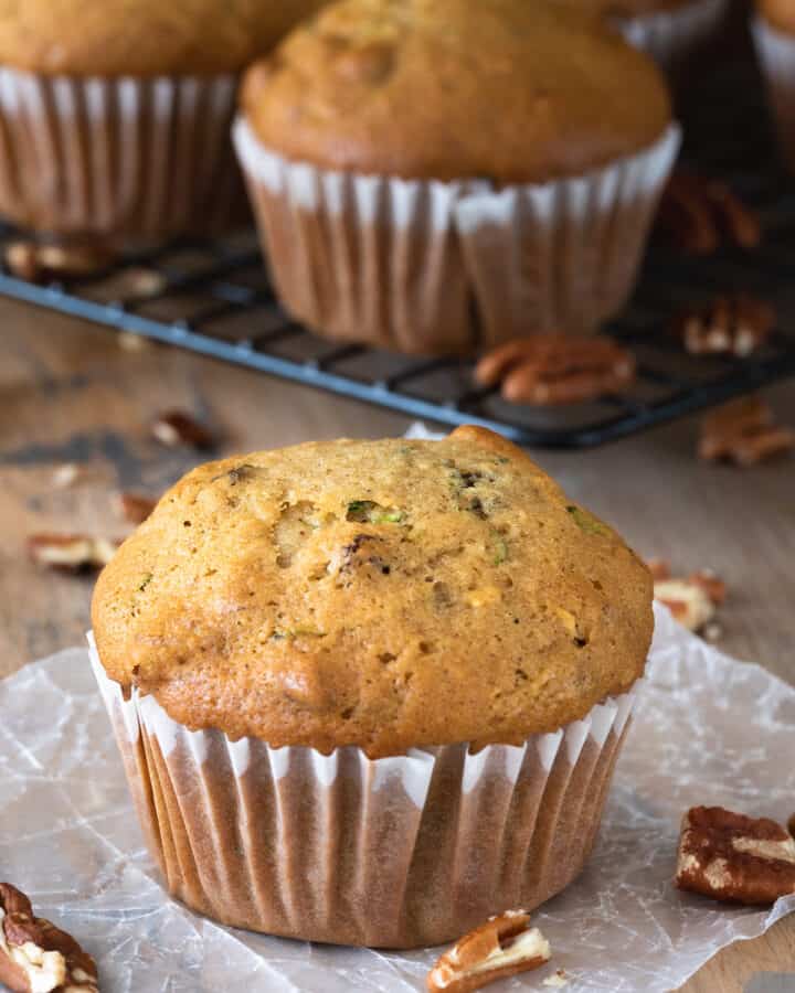 Zucchini Muffin in a paper wrapper with several muffins in the background.