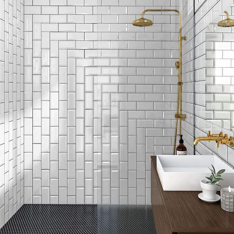 White subway tile shower with dark grey floor in a unique pattern. Gold accents for shower head.