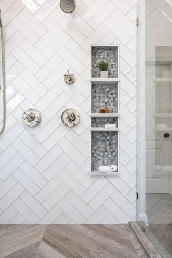 Double herringbone tile shower wall with darker grey niche holding toiletries.