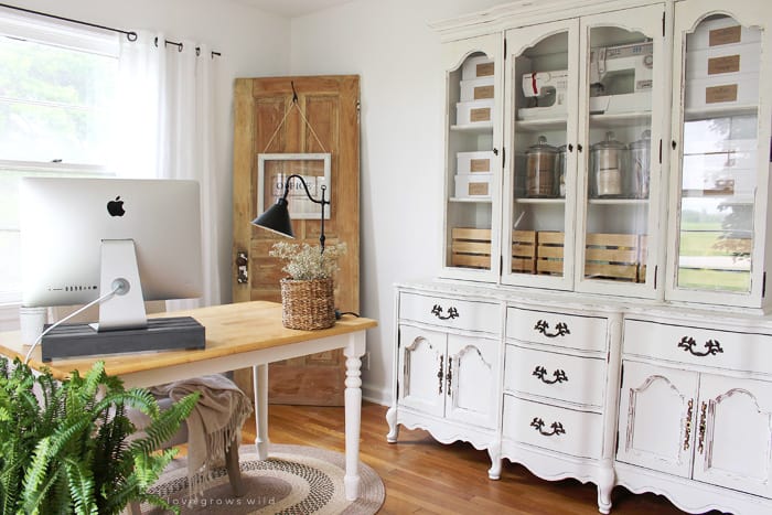 White farmhouse dining room with large display hutch that has craft supplies in it and glass jars.