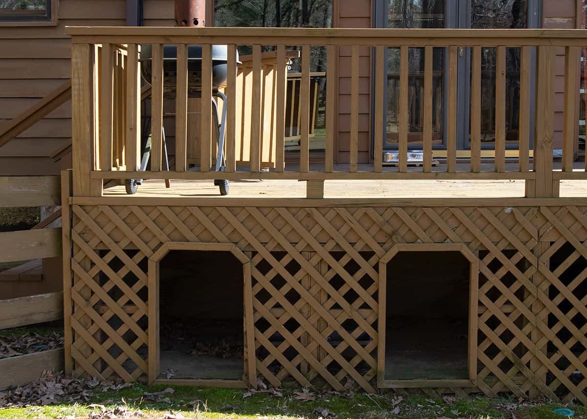 Wood stained deck with two cubbies cut out of lattice and framed for dog houses.