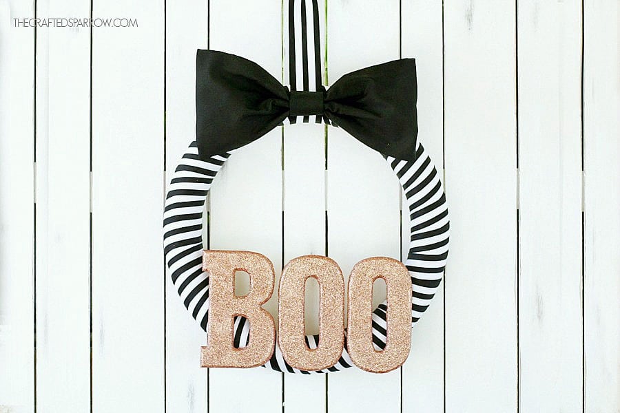 Black and white ribbon wreath with BOO in the center in metallic gold.