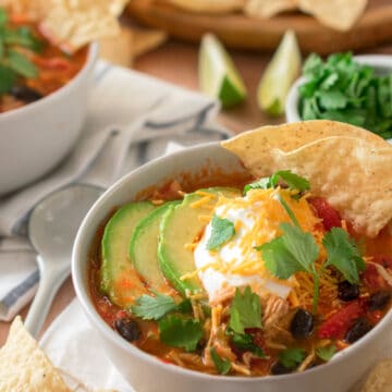 Chicken Tortilla Soup in a bowl topped with sour cream, avocado, cilantro, and cheddar cheese.