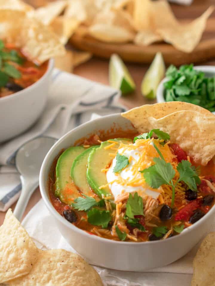Chicken Tortilla Soup in a bowl topped with sour cream, avocado, cilantro, and cheddar cheese.