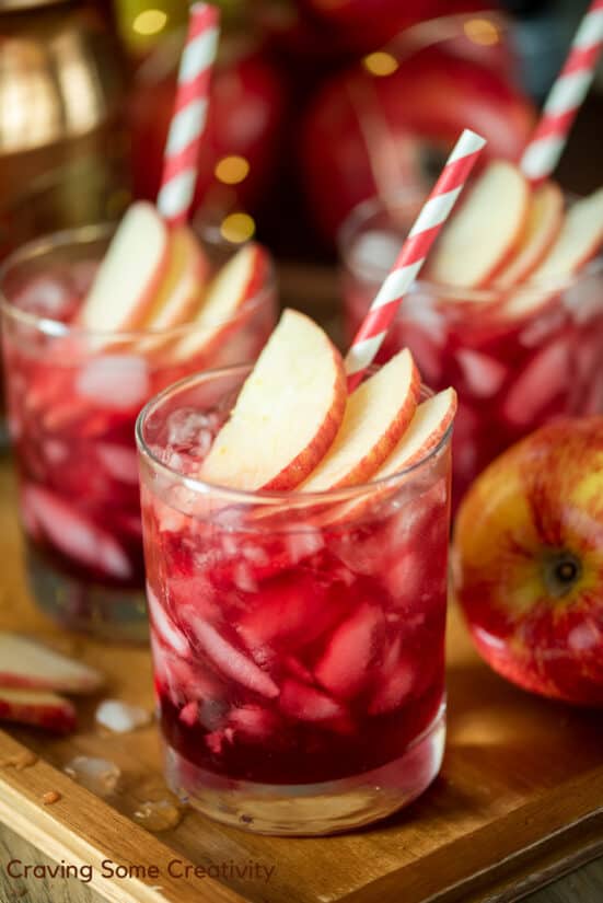 Apple cocktail with crown royal and pomegranate juice with apples and red striped straws for garnish.