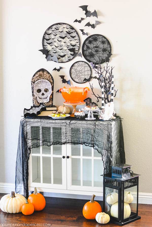 Halloween decorated buffet table with skulls, pumpkins, and a draped black scarf.