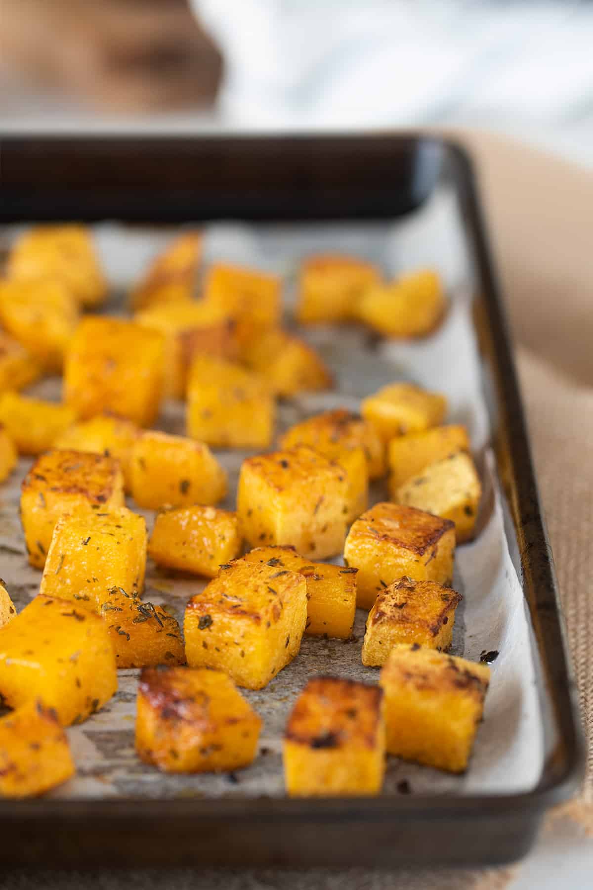 Cubed roasted butternut squash on a dark sheetpan.