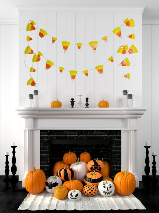 White mantle with candy corn banner and a pile of decorated pumpkins spilling out of the fireplace.