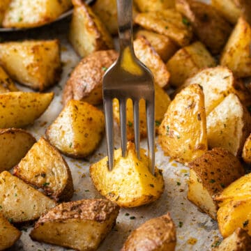 Oven roasted potatoes with Cajun seasoning on a pan with a fork in one wedge.